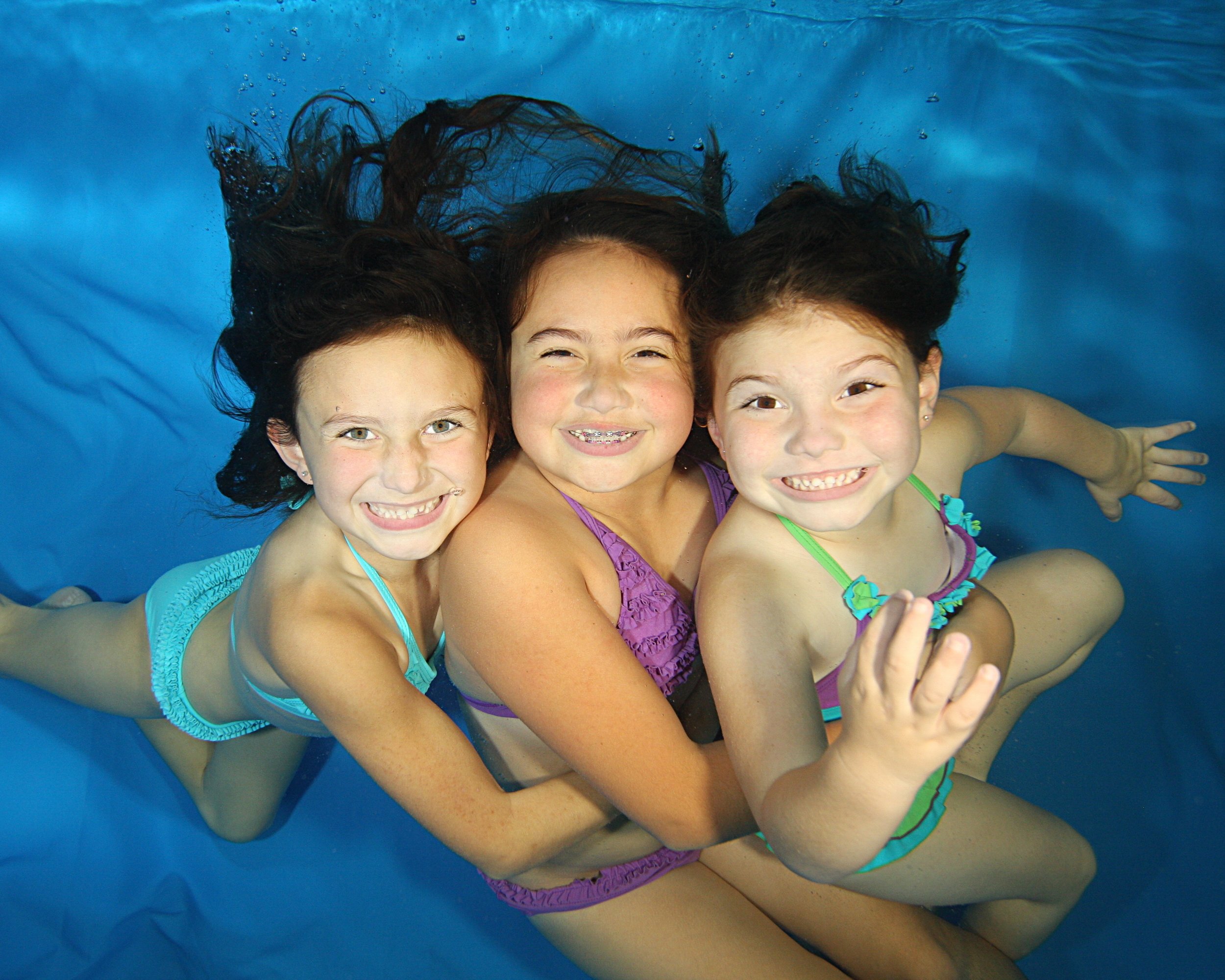Three young girls swimming under the water while smiling at the camera